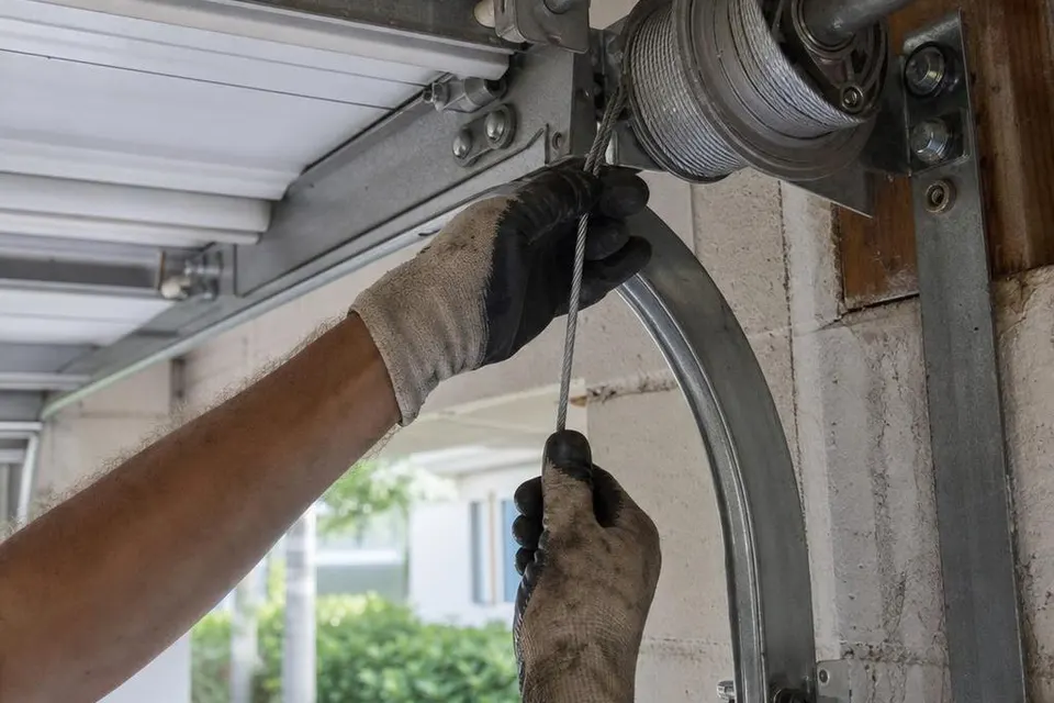 Technician replacing a garage door lift cable beside the cable drum