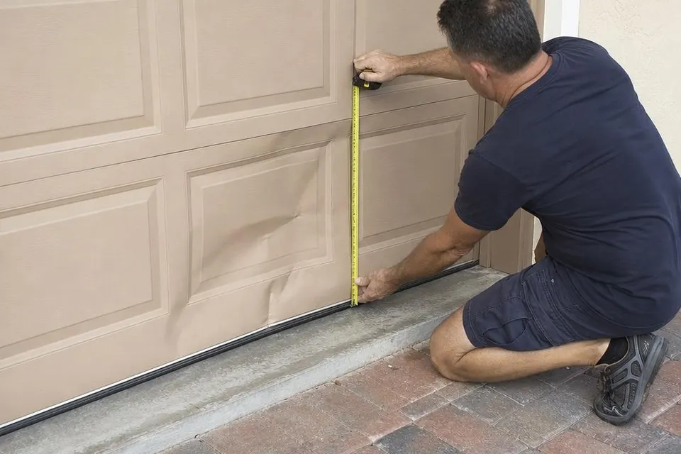 Technician measuring damage on a dented garage door panel